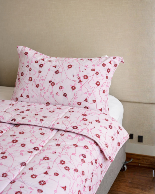 Cubrecama rosado con estampado floral rojo sobre una cama