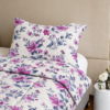 Cubrecama hueso con estampado floral morado sobre una cama