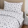 Cubrecama blanco con estampado triángulos chiquitas color azul sobre una cama