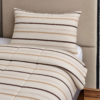 Cubrecama beige con estampado líneas marrones sobre una cama