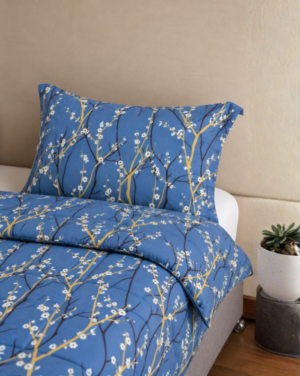 Cubrecama color azul jean con estampado de ramas mostazas sobre una cama